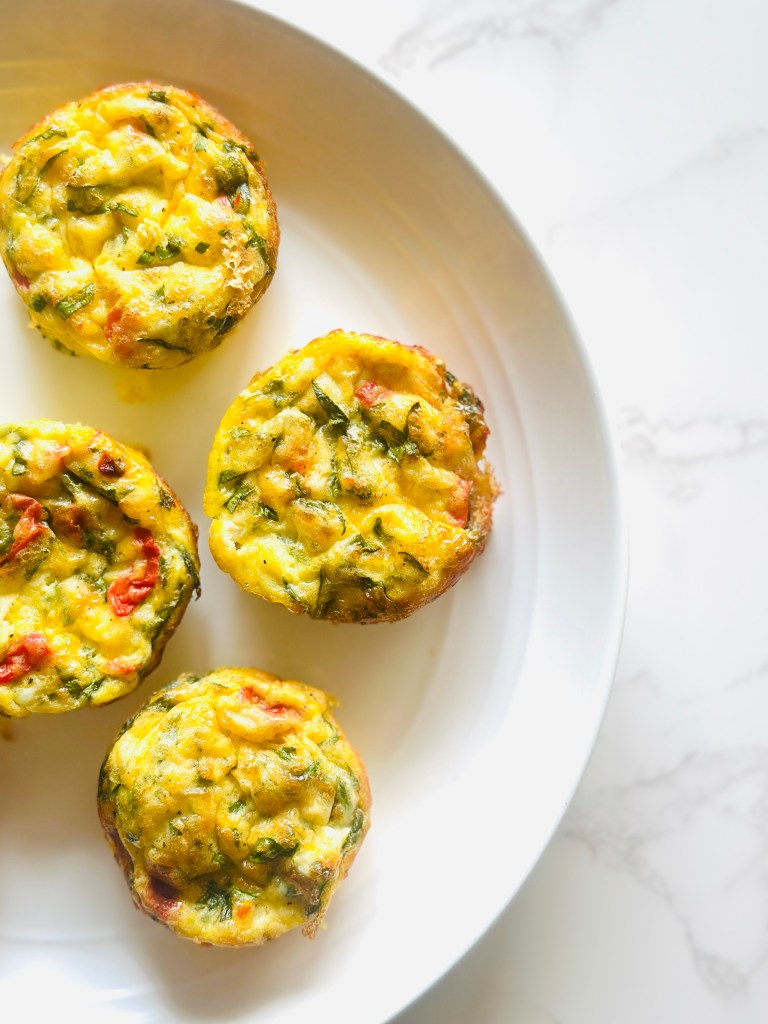 A white platter of cottage cheese egg bites, made with eggs, cottage cheese, spinach, roasted pepper, and shredded Mexican cheese