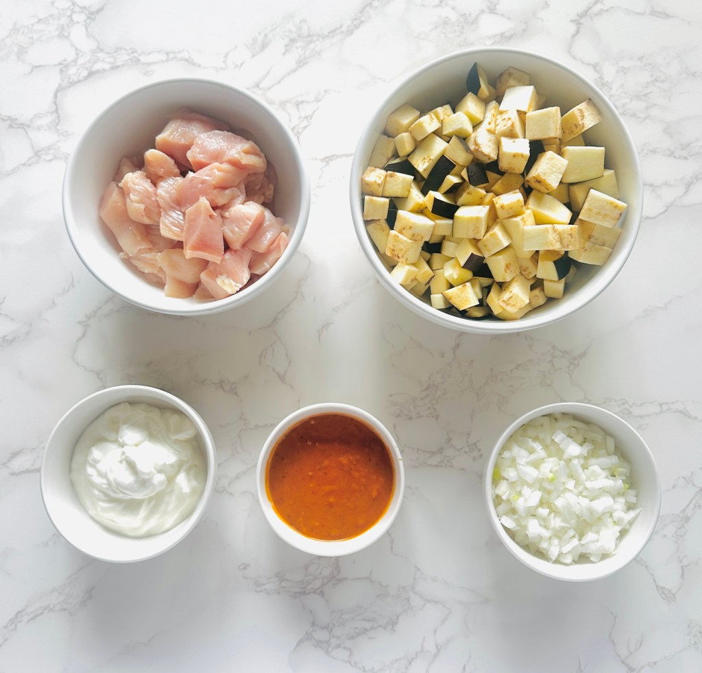 A photo of ingredients used to make chicken eggplant curry: chicken breasts, eggplant, yellow onion, Greek yogurt, and spicy curry sauce