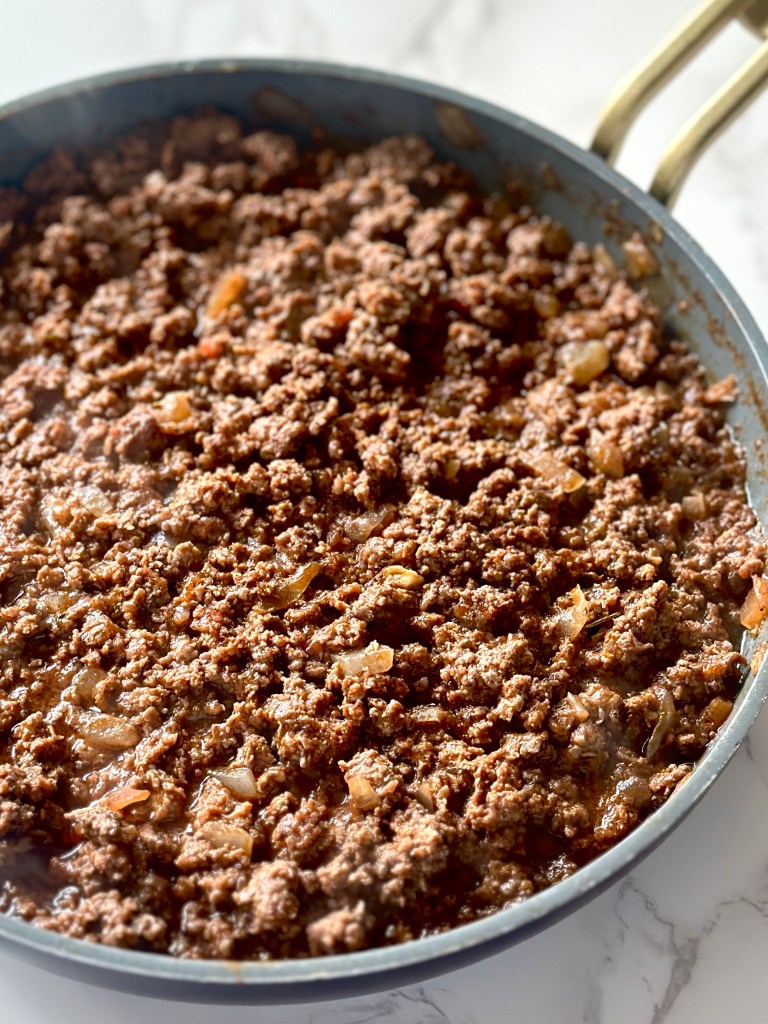 A skillet of cooked ground beef with onion, oregano, Italian seasoning, garlic powder, cumin, salt, and black pepper