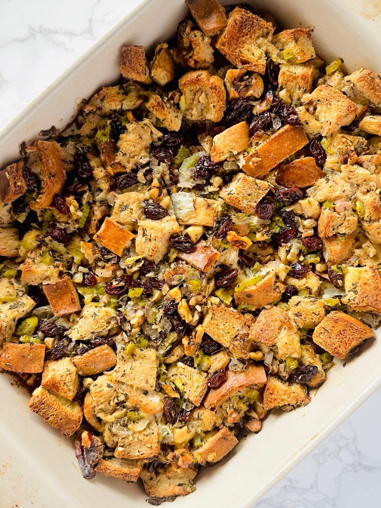 A baking dish containing a layer of Thanksgiving stuffing, made with onion, celery, raisins, walnuts, and bread cubes