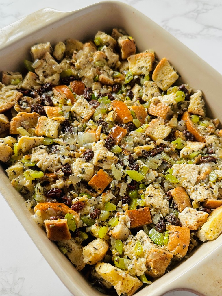 A baking dish containing a layer of Thanksgiving stuffing, made with onion, celery, raisins, walnuts, and bread cubes