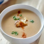 A serving bowl of roasted cauliflower soup, topped with cauliflower florets, chopped parsley, and ground allspice