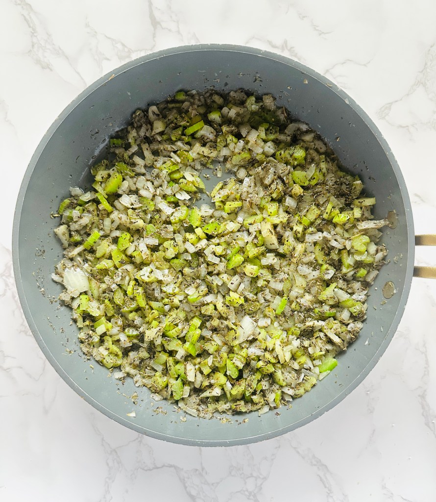 Chopped onions and celery being sautéed with butter in a large skillet