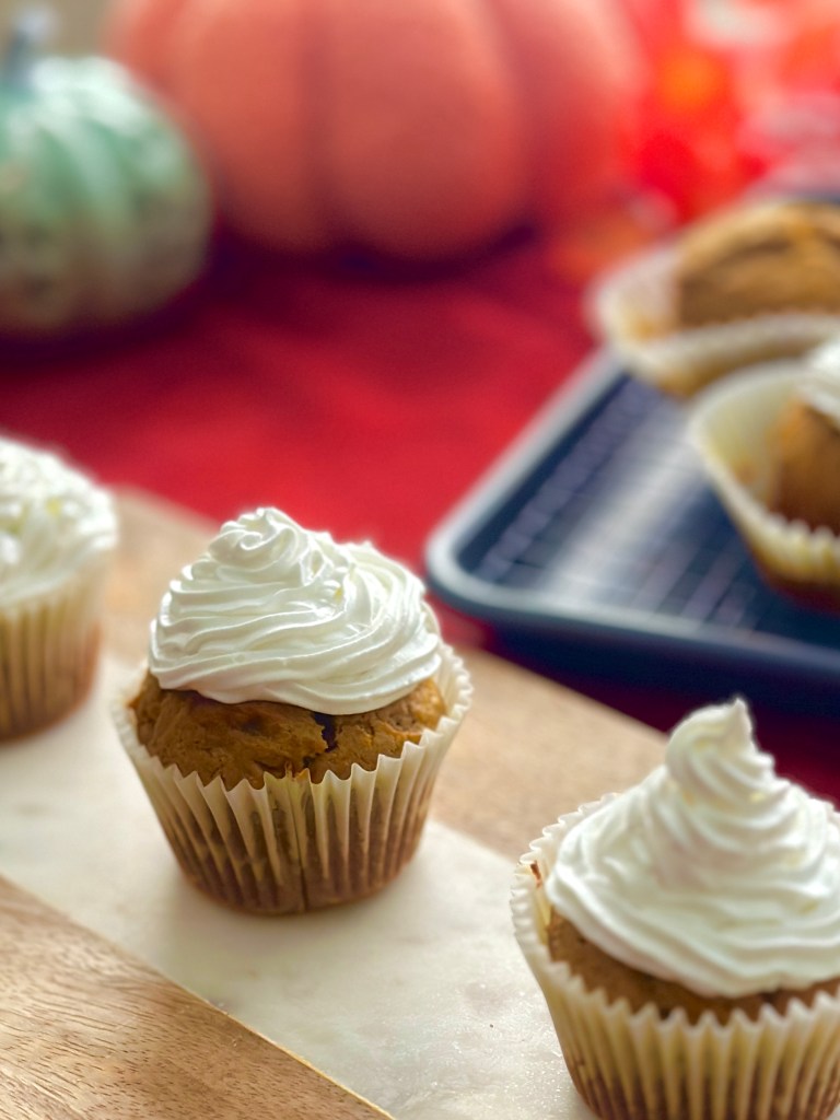 Homemade pumpkin cupcakes on a serving board with a whipped cream topping