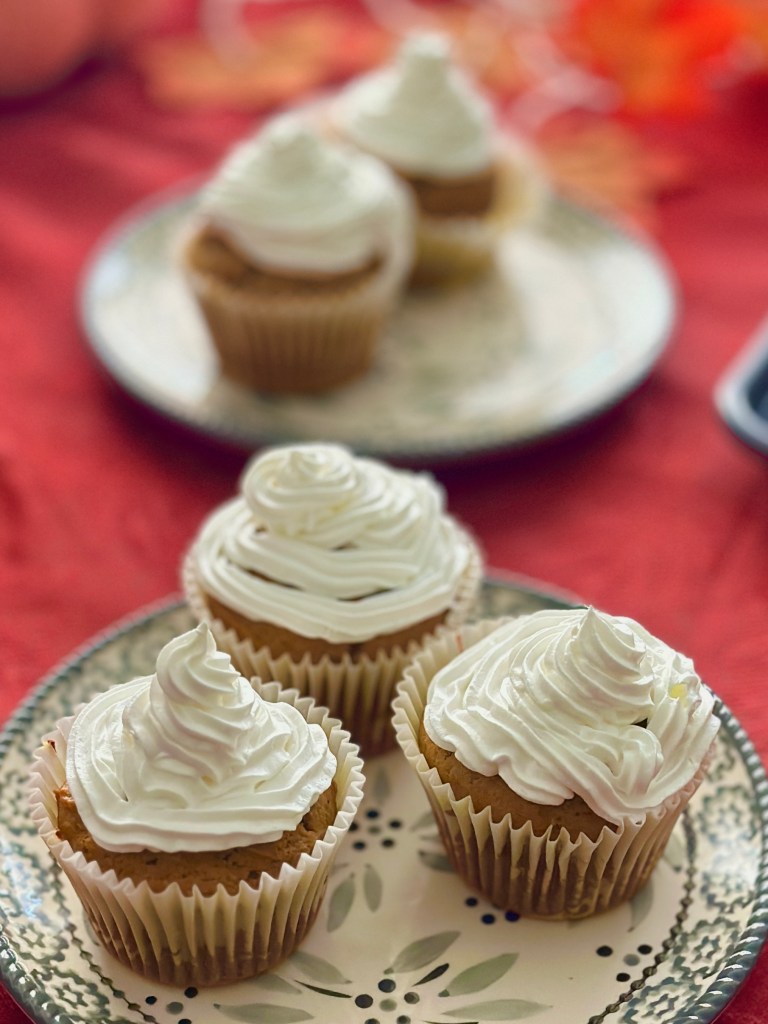 Homemade pumpkin cupcakes on serving plates with a whipped cream topping