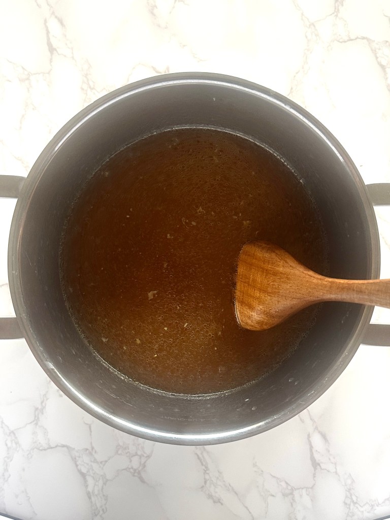 A stainless steel soup pot full of cooked onion, garlic, and 4 cups of vegetable broth