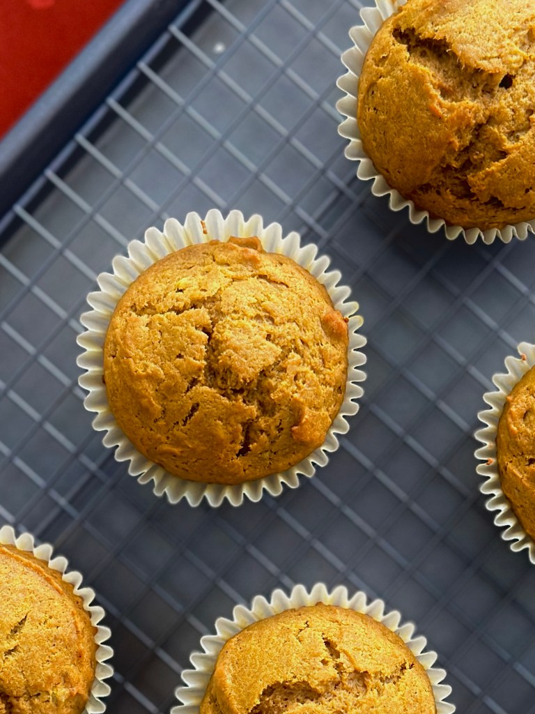 A sheet tray topped with a wire rack containing freshly baked pumpkin cupcakes